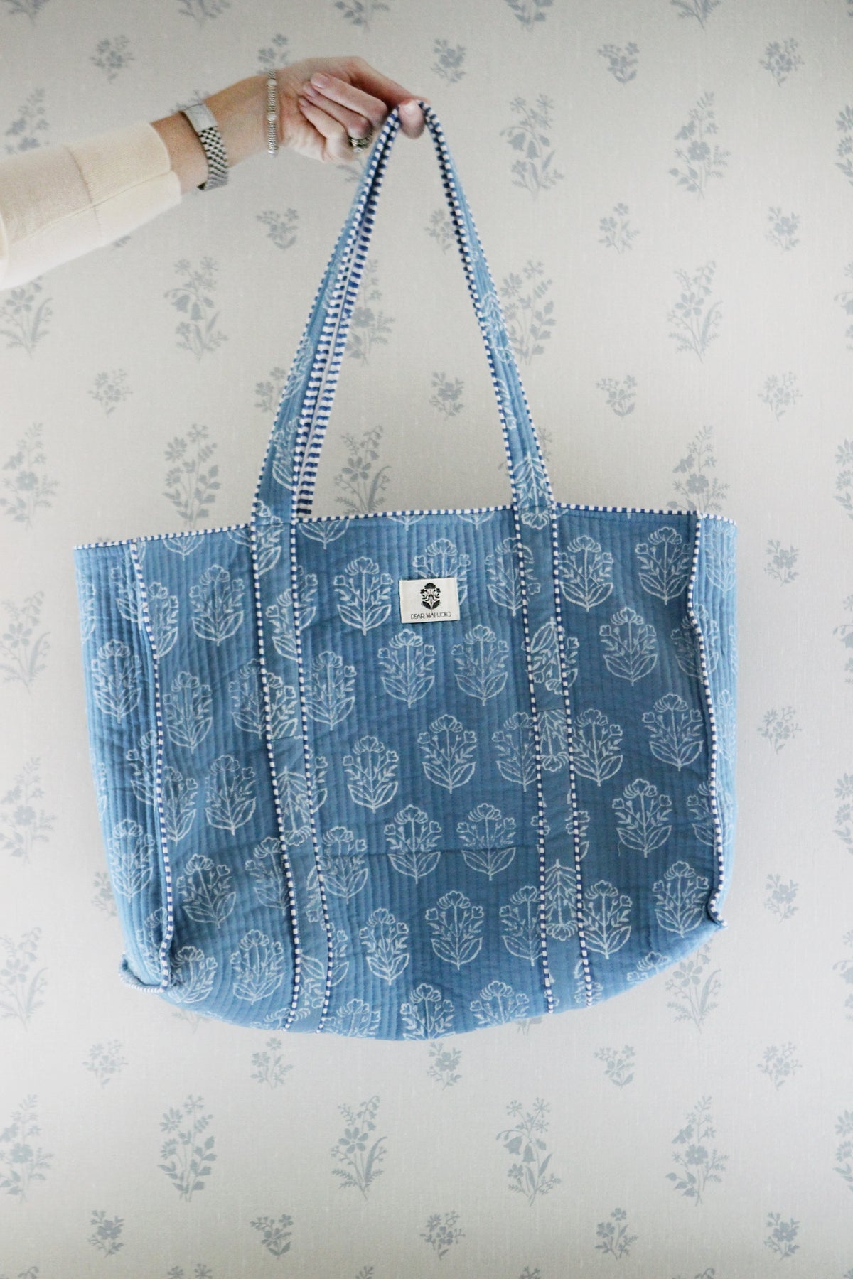 French blue block-print quilted mahjong tote held up against floral wallpaper