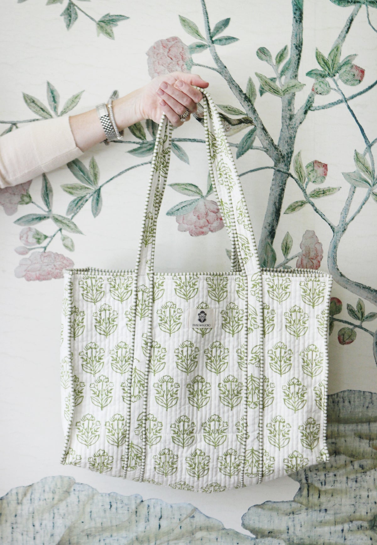 Pistachio block-print quilted mahjong tote held up against floral wallpaper